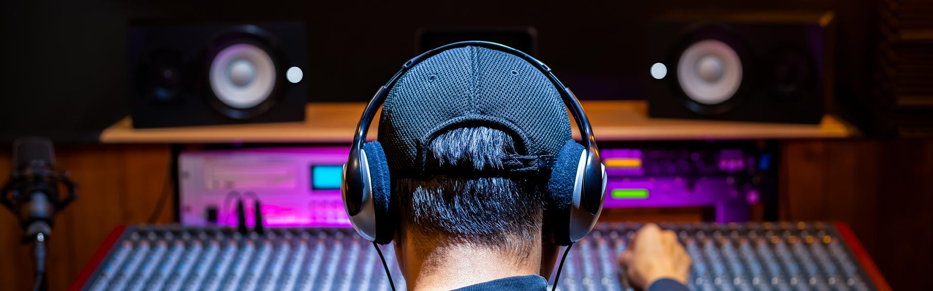 back of asian male professional music producer, sound engineer mixing a song on audio mixing console in recording studio. music production, post production concept