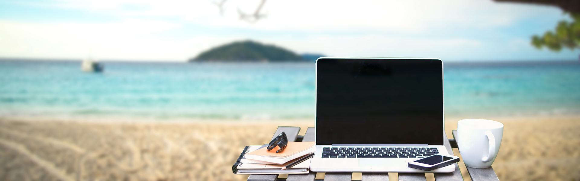 Front view of cup and laptop on table in Office park and blurred background of the beach in the summer, Similan, Thailand