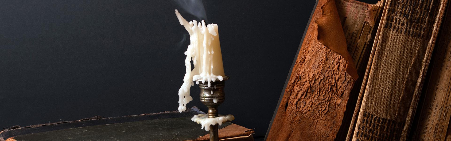 Stack of ancient books and candlestick with steaming candle