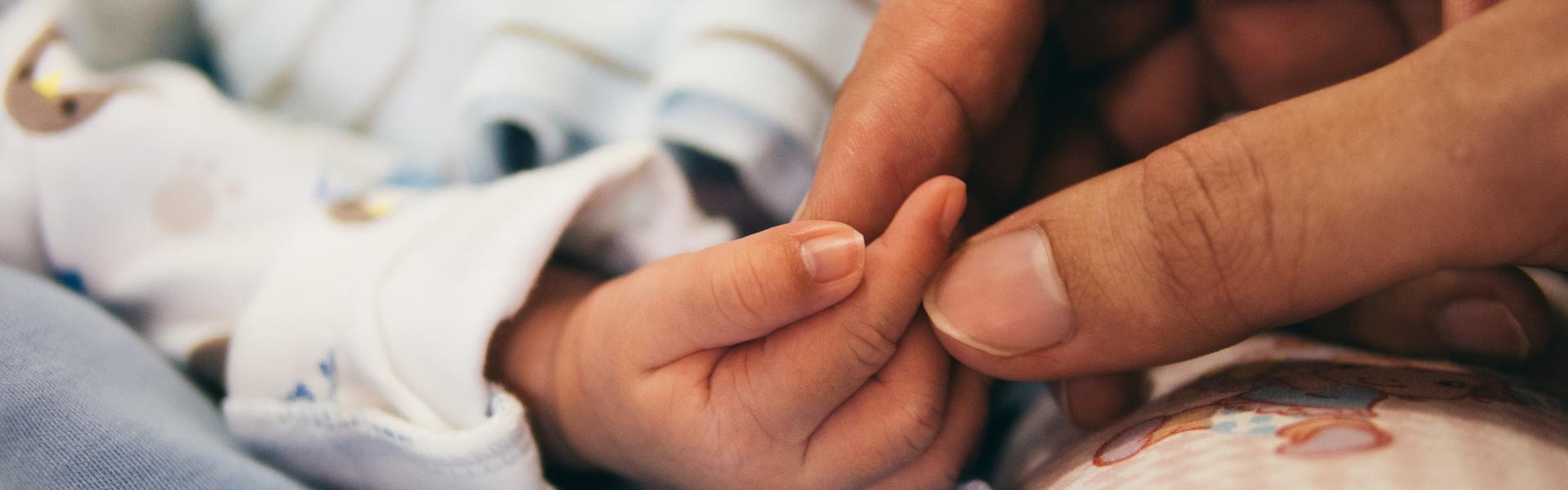 A nurse holding the hand of a newborn baby.