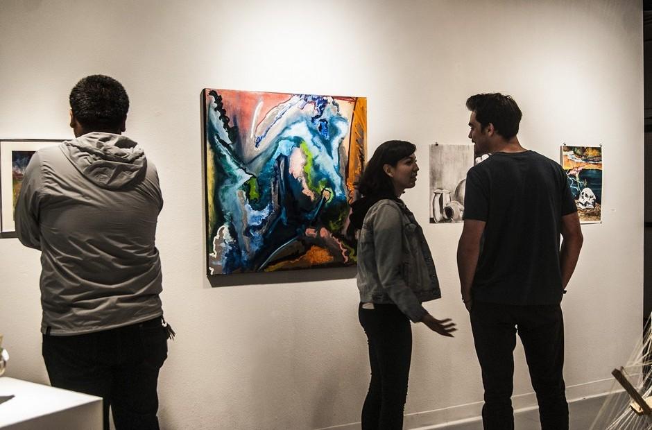 Several people looking at paintings on a wall.