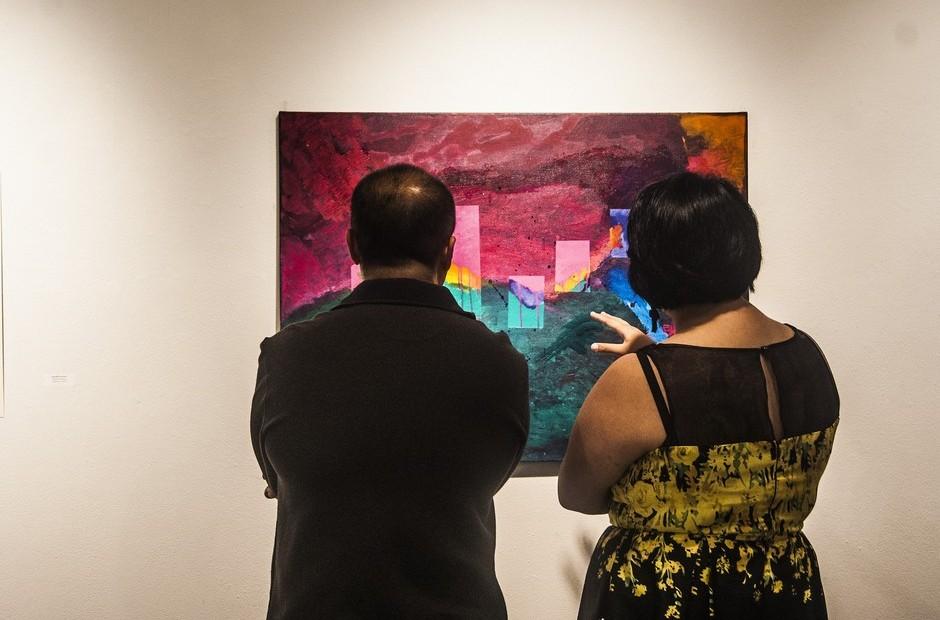 Two peopel looking at a painting on the wall.