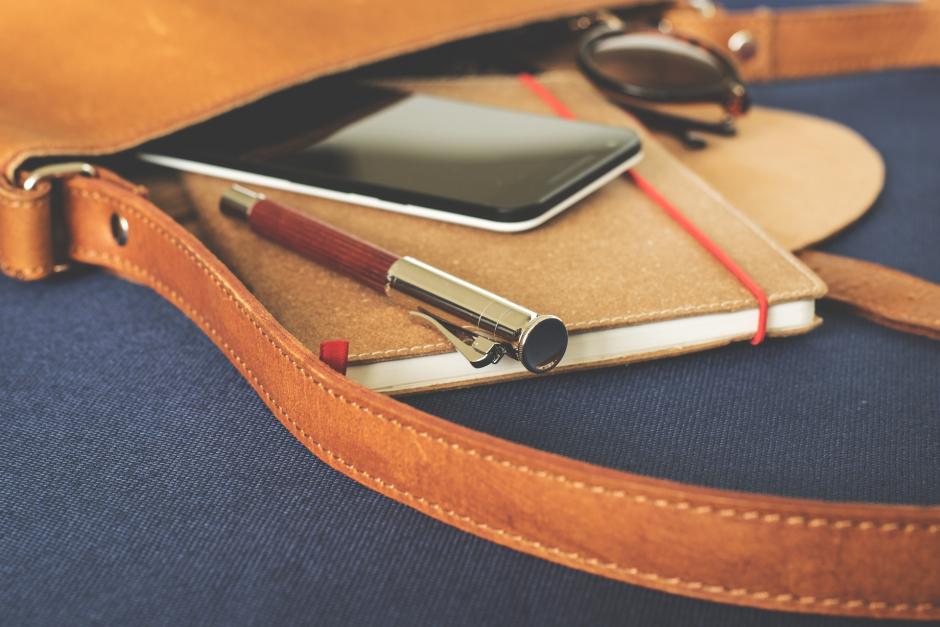 Book bag with notebook, pen, and pencil sliding out of bag. 