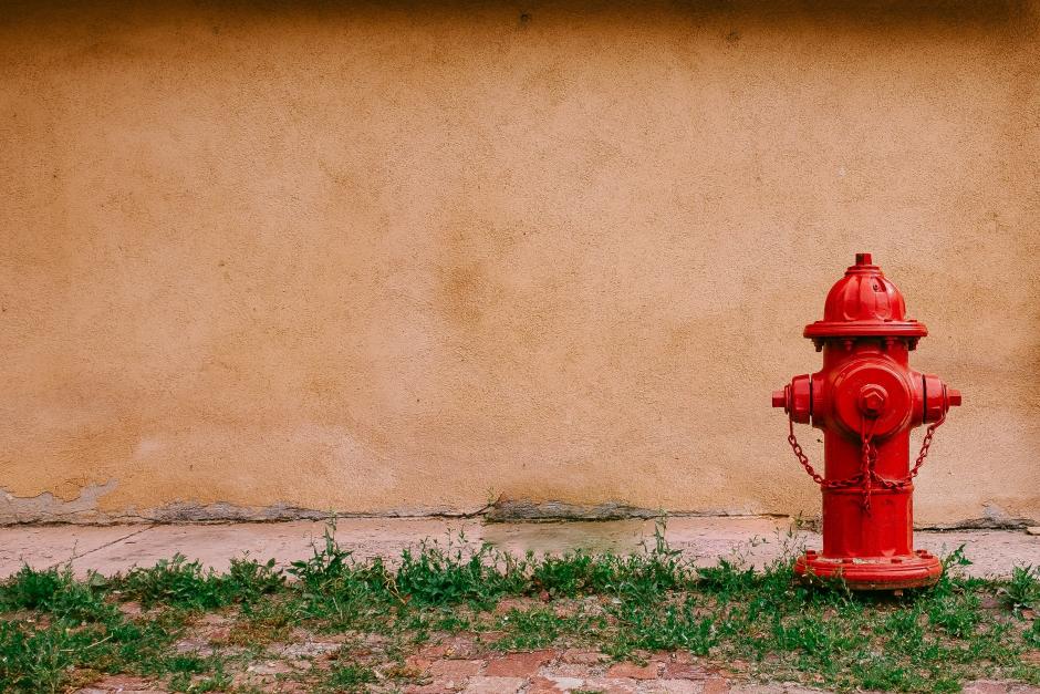 a picture of red fire hydrant in front of a wall