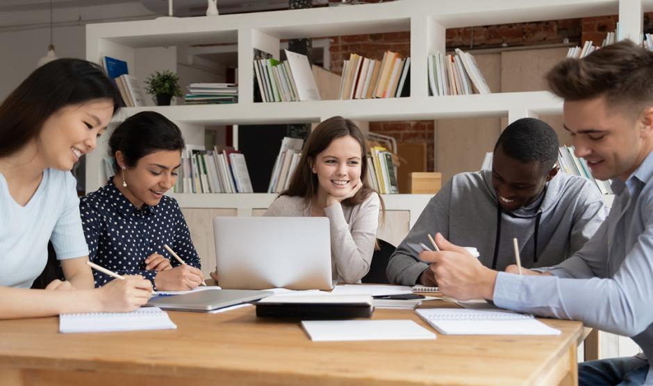 Multi-racial students study together seated at library desk 