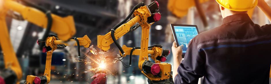 A men operating at Manufacturing Factory producing goods with Robotic Arms and computer device.