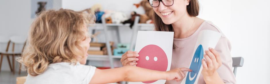 Smiling counselor holding pictures during meeting with young patient with autism