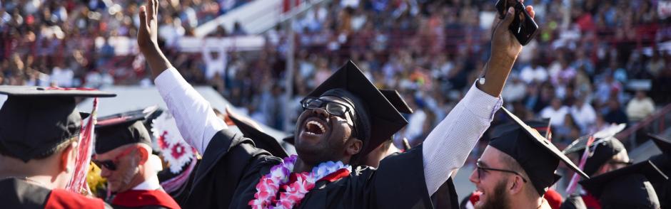 A black, college student cheering at his graduation.