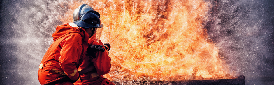 Firefighter in fire fighting suit spraying water, Firemen fighting raging fire with huge flames of burning, Fire prevention and extinguishing concept