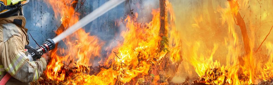 Firefighter in fire fighting suit spraying water, Firemen fighting raging fire with huge flames of burning, Fire prevention and extinguishing concept
