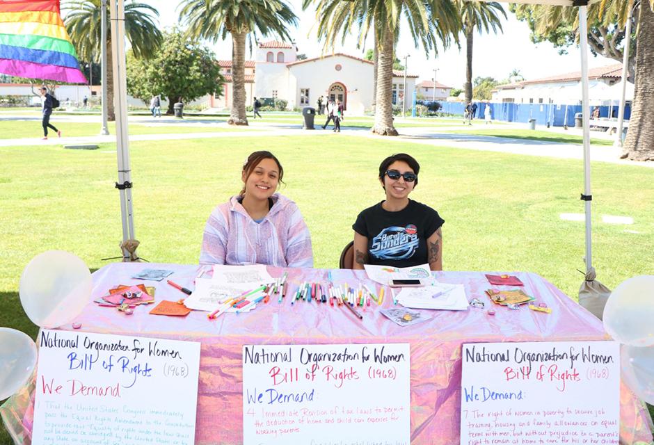 two LBCC students sitting at the Feminist Student Club booth table recruiting for new members