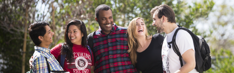 Six students smiling outside while holding another student in their arms.