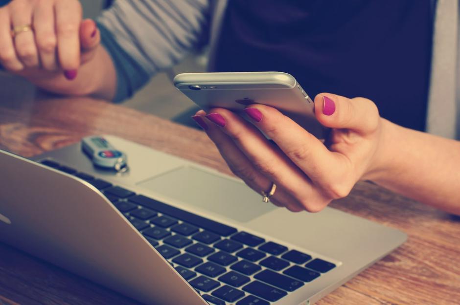 holding cell phone next to laptop