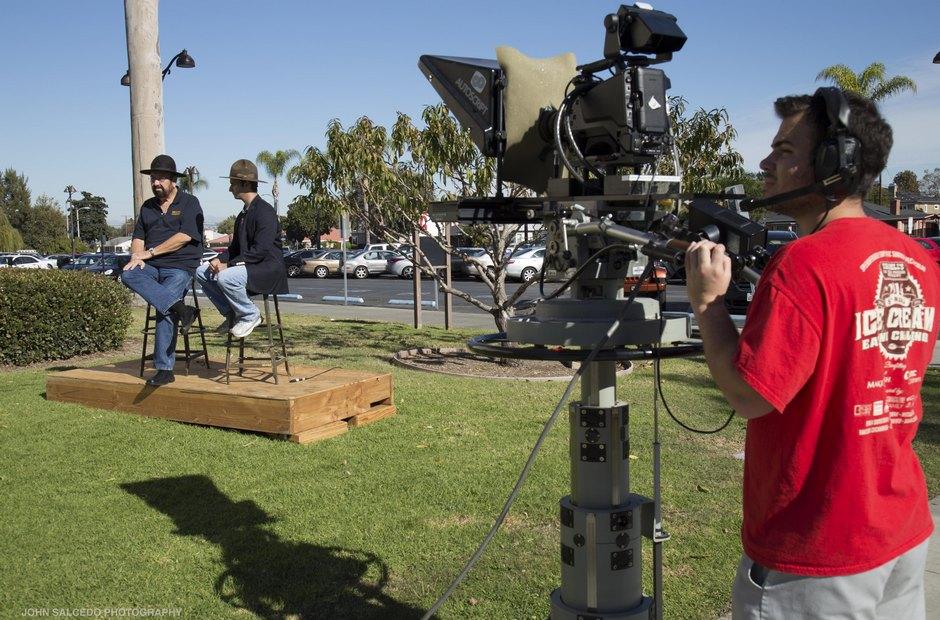 A cameraman filming outside on the grass.