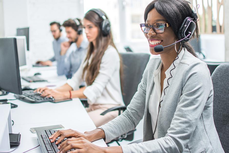 Customer Support worker smiling while chatting with customers on the phone infront of computers