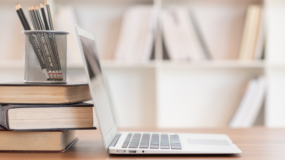 Laptop with books on desk. Cup of pencils. 