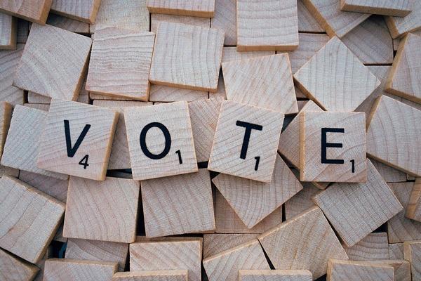 The word "VOTE" spelled with Scrabble tiles.