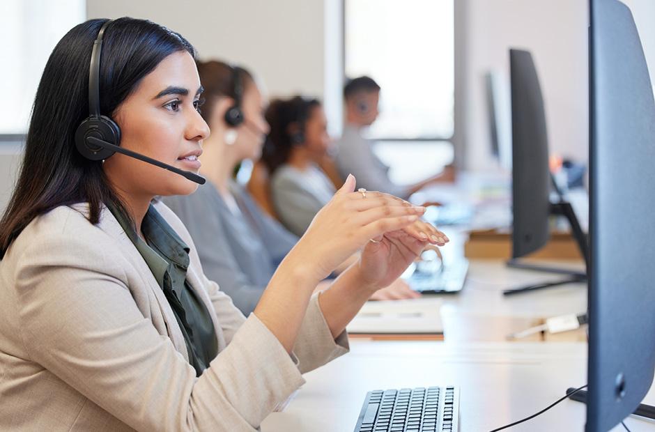 An image of a young call center agent working in an office with her colleagues