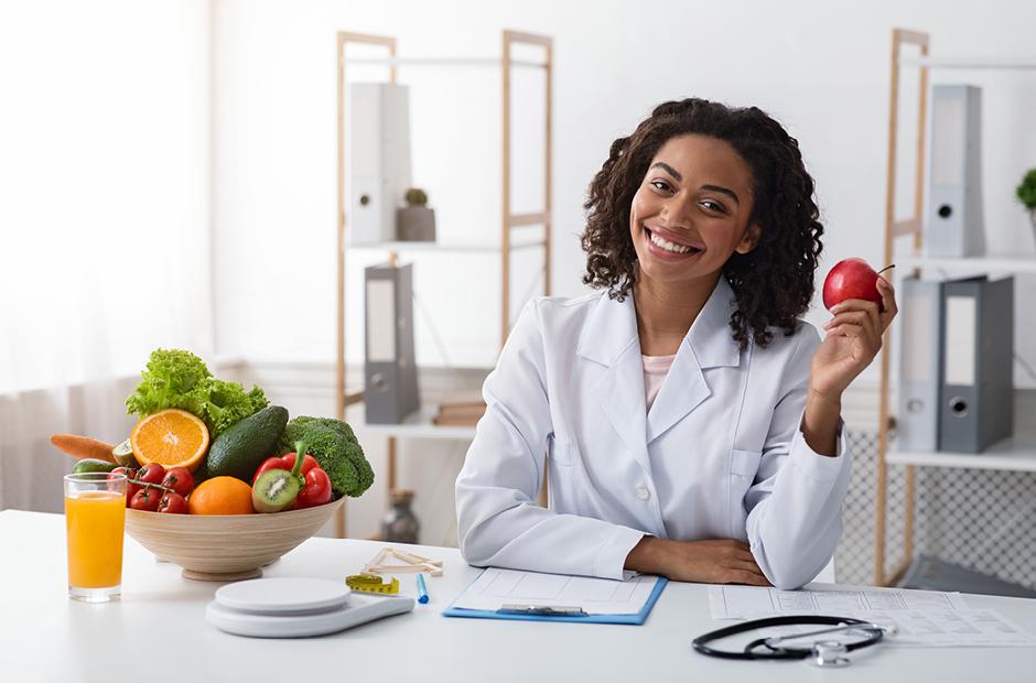 Pretty female dietologist holding apple in her hand and smiling 