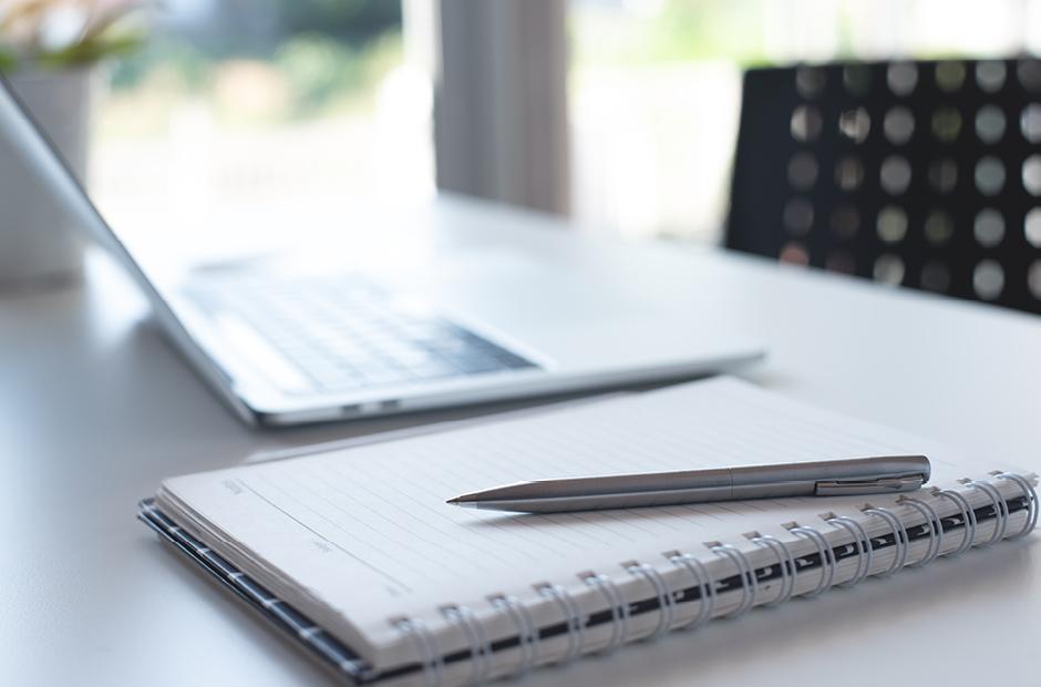 Pen, paper notebook and laptop computer on white office table with no people, blurred for business background