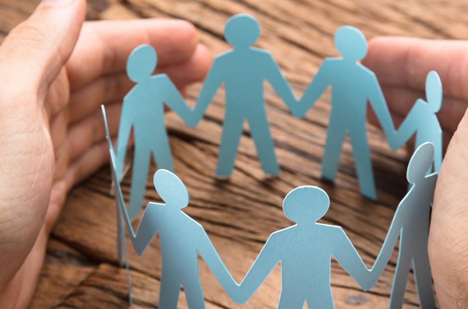 Cropped image of businessman's hands covering paper team on wooden table