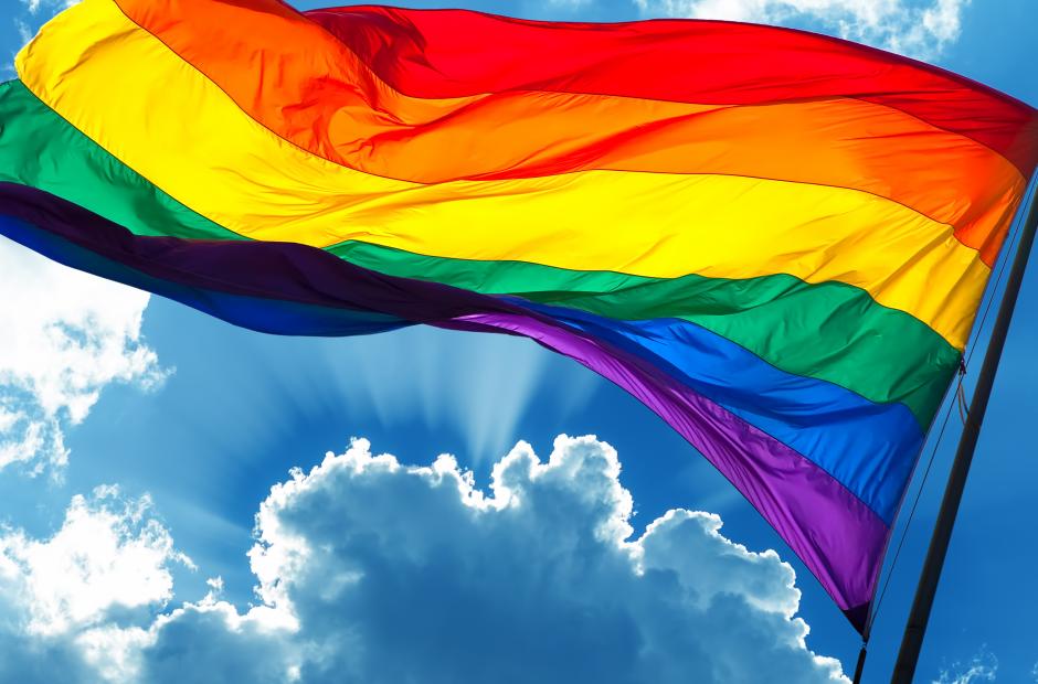 Rainbow flag on cloudy sky background