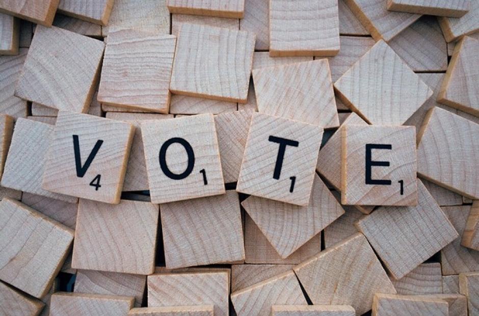 The word "VOTE" spelled with Scrabble tiles.
