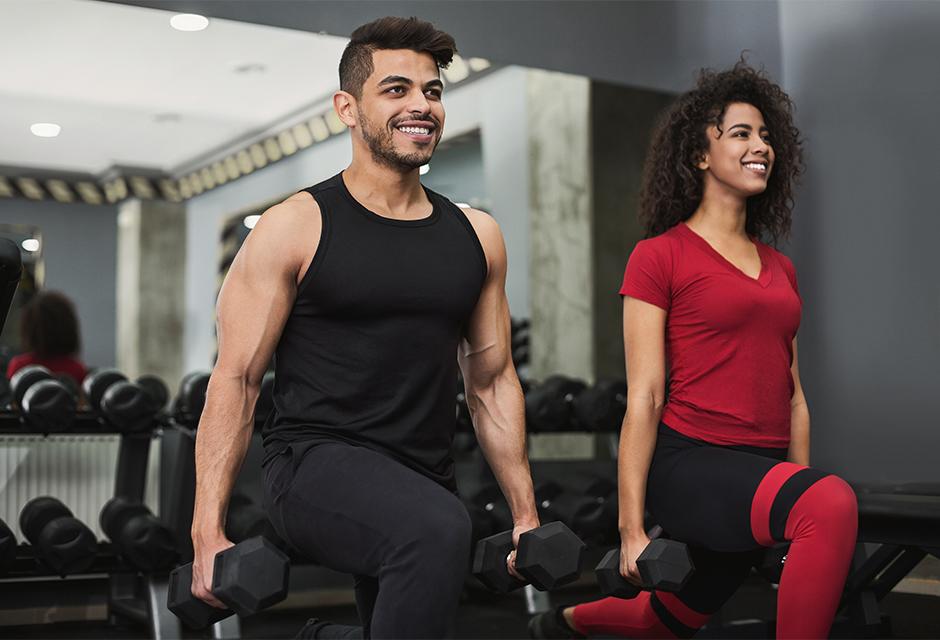 Diverse couple training with dumbbells in gym