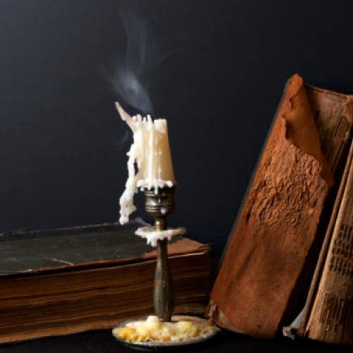 Stack of ancient books and candlestick with steaming candle