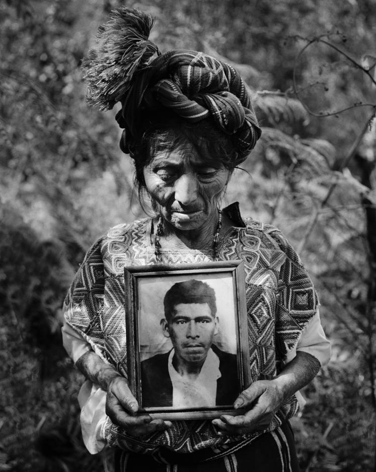A survivor of the Guatemalan Genocide carrying a framed photo