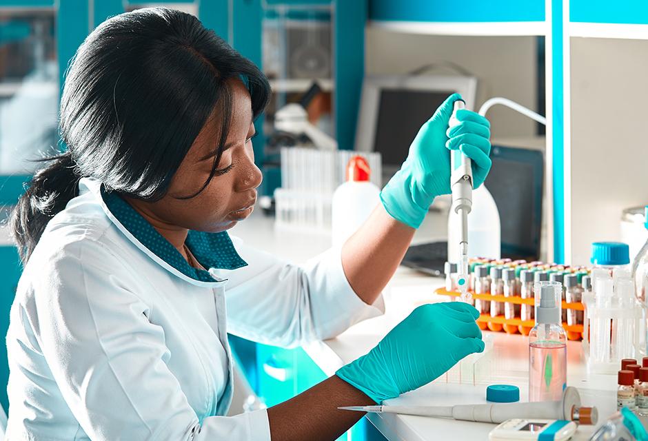 African scientist or graduate student in lab coat and protective wear performs PCR testing of patient samples in modern test laboratory. Developing pcr kits to diagnose Covid-19 patients.