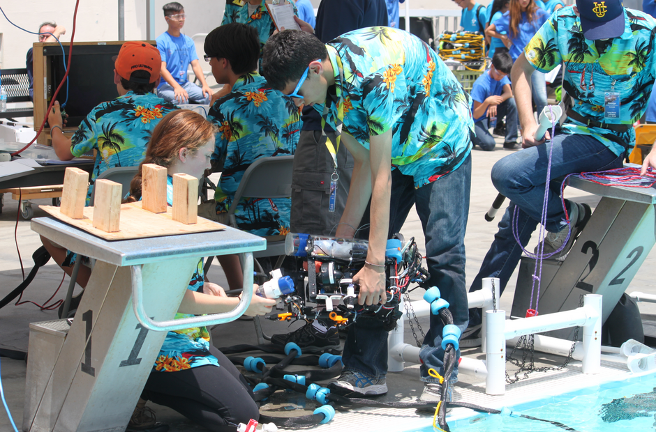 Students working on an underwater robot near a pool.