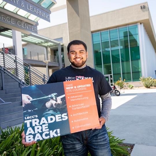 An LBCC student holding a poster announcing the Traded are back to the school of Career Technical Education 