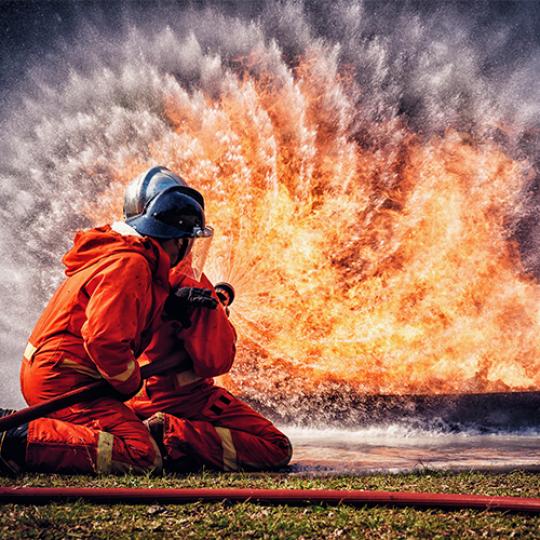 Firefighter in fire fighting suit spraying water, Firemen fighting raging fire with huge flames of burning, Fire prevention and extinguishing concept