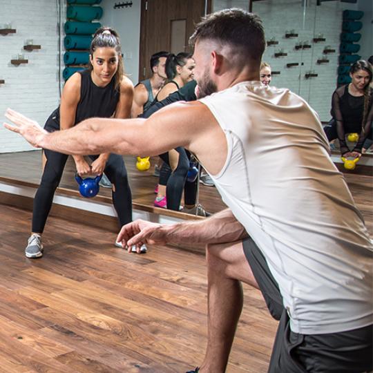 Panoramic view of sporty people training with weights with assistance of their coach at health club